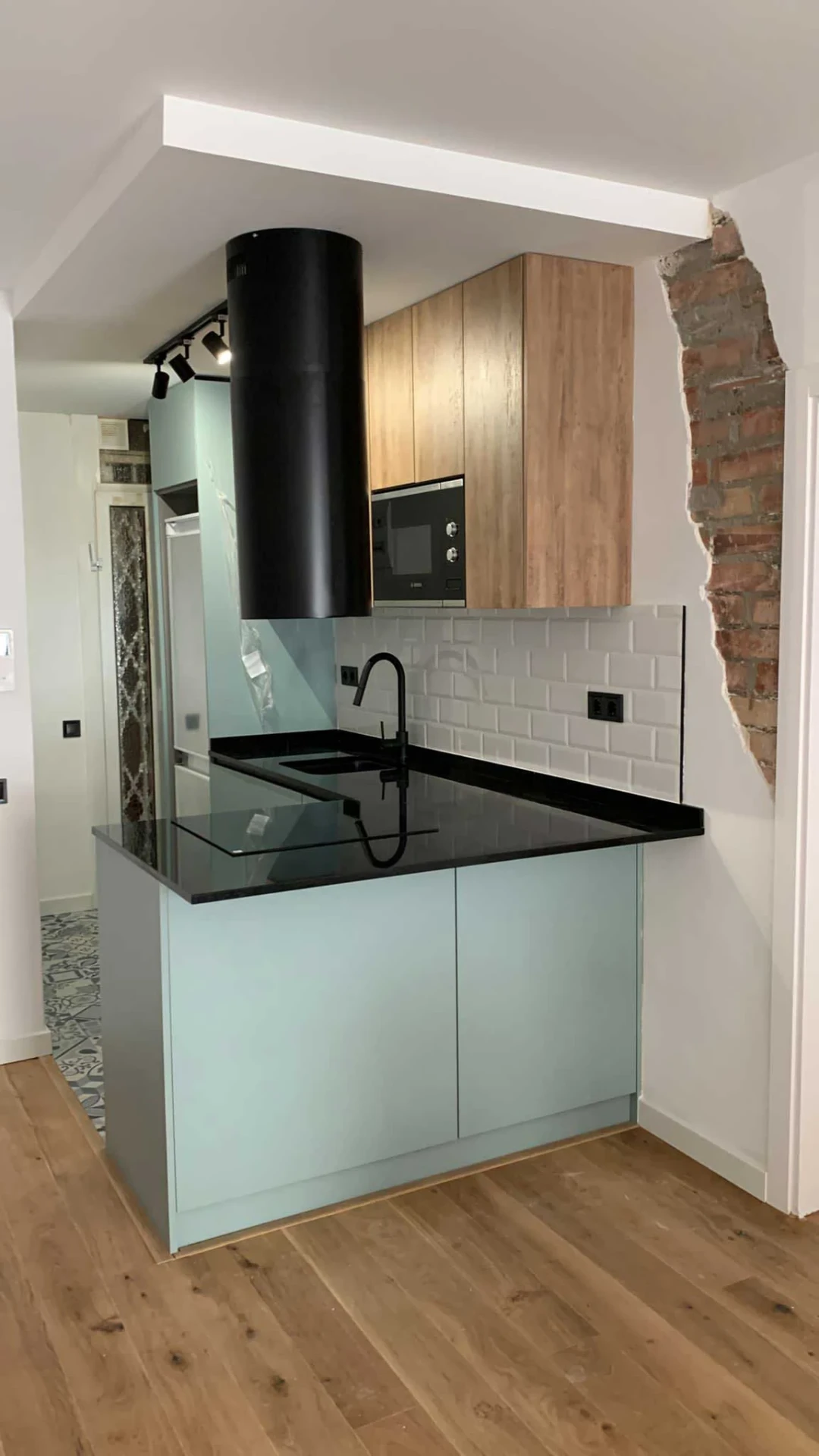 Cocina con isla azul, encimera negra y pared de ladrillo visto